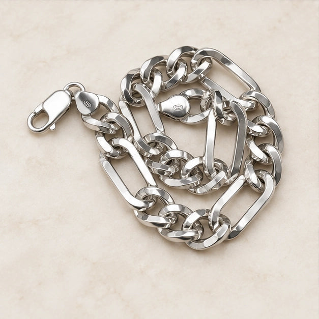 Polished alternating elongated rectangular links and shorter rounded curb links, lobster clasp. On an ivory background