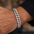 Polished flat curb-link chain with lobster clasp. Worn on an adult wrist with ivory linen
