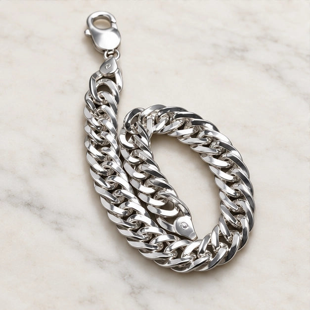Polished flat curb-link chain with lobster clasp. On an ivory background