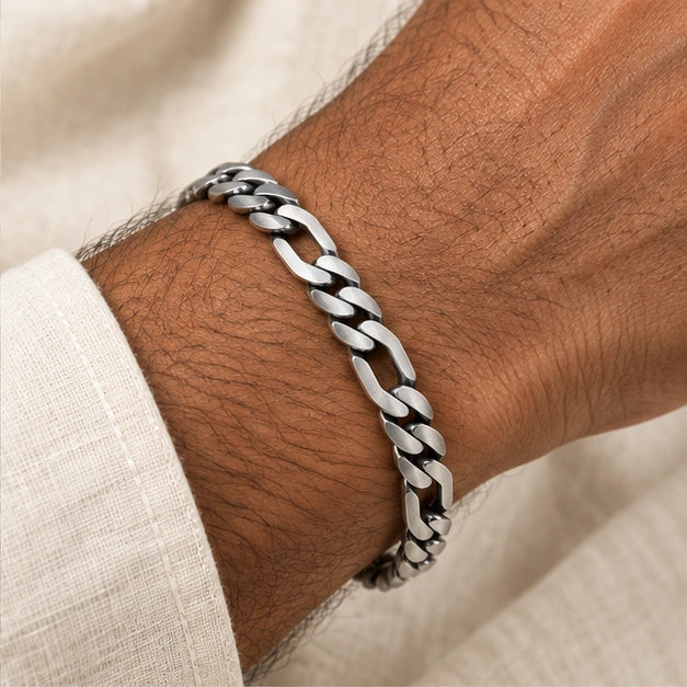 Flat alternating curb and elongated link bracelet worn on an adult wrist beside ivory linen